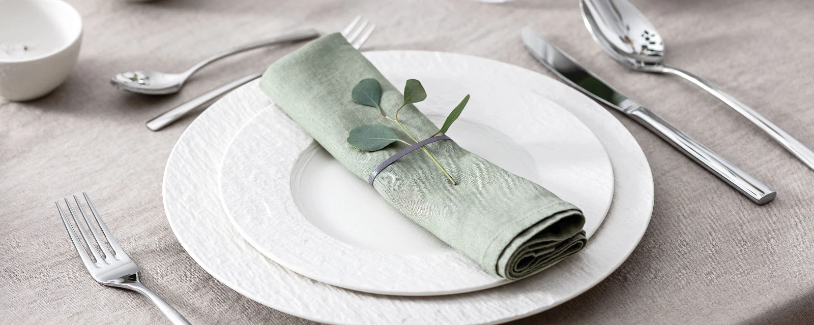 A set table with two white Manufacture plates, pastel green napkin, Piemont flatware and eucalyptus.