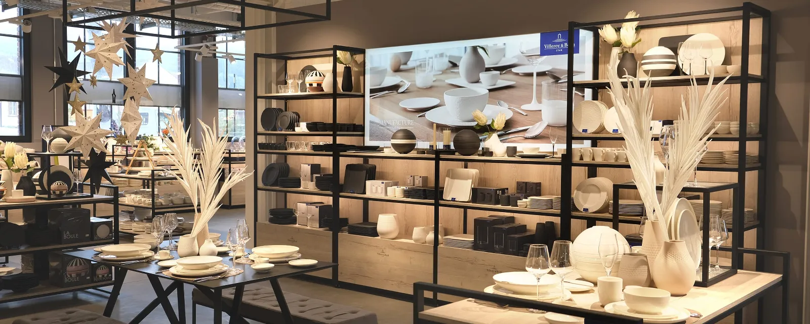 Modernes Ladeninterieur mit vielfältigen Keramikgeschirren Modernes Ladeninterieur mit vielfältigen Keramikgeschirren und Dekor auf schwarzen Metallregalen und Tischen mit sanfter Beleuchtung.