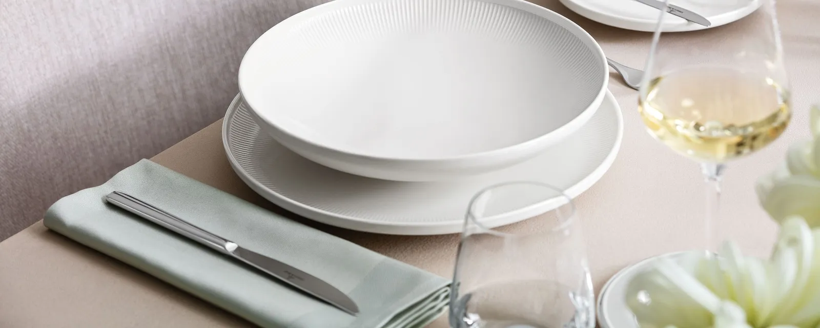 A table with a glass of wine and a table set with Villeroy & Boch Afina plates.