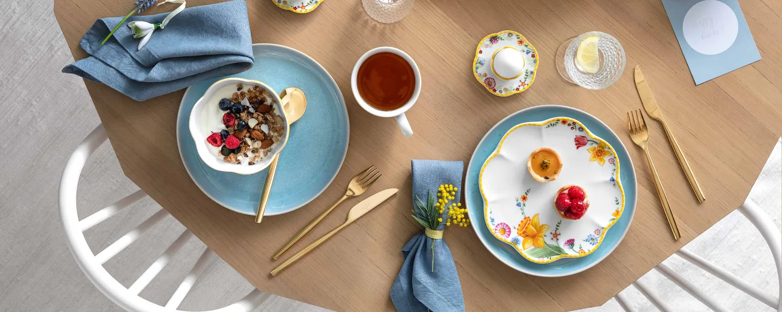 Une table printanière décorée avec de la vaisselle Spring Awakening et Crafted, un kouglof, un plat creux rempli de flocons d’avoine avec des baies, une tasse de thé et des œufs décoratifs.