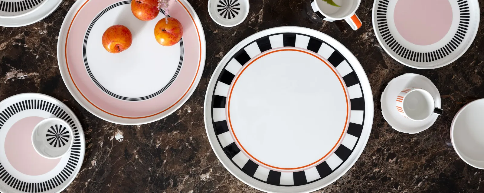 Memphis in all its facets Memphis table setting by Villeroy & Boch with decorative plates, a mug, cups and plums on a brown marble surface decorated with bright flowers.