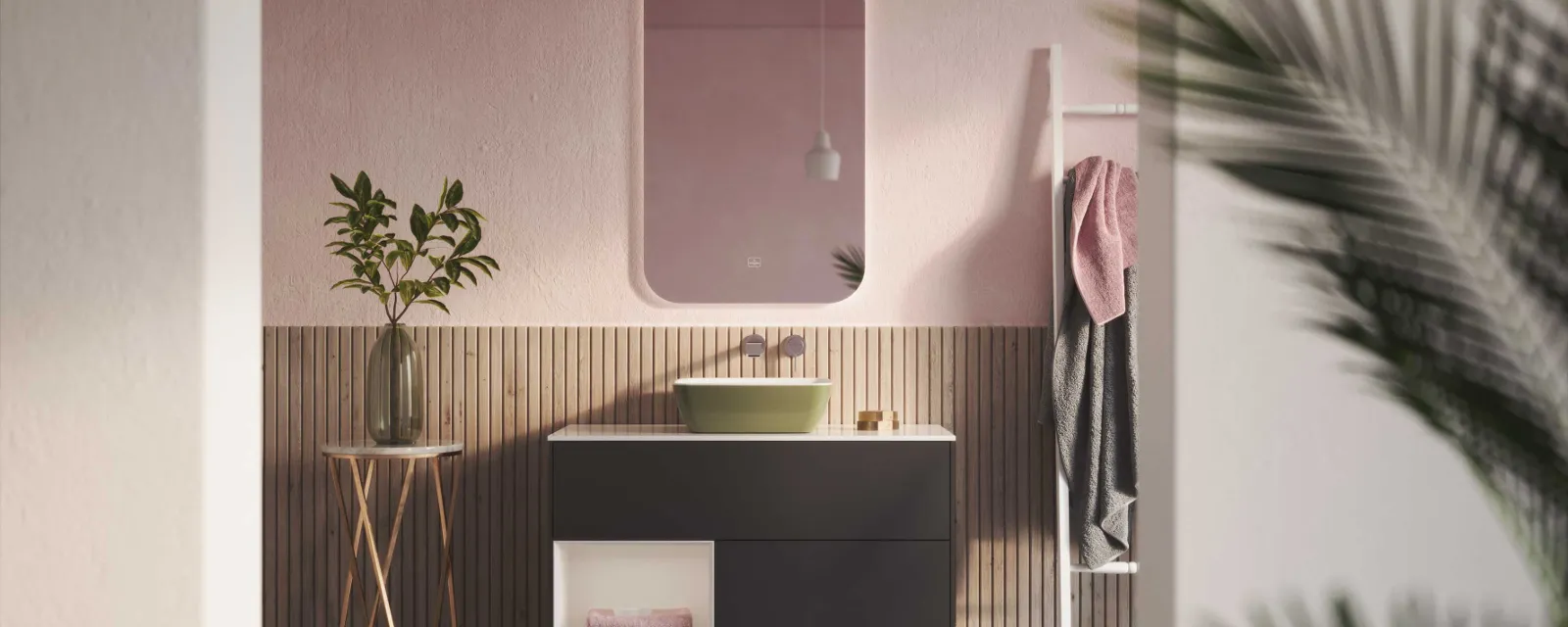 Modern bathroom with a Villeroy & Boch green Artis washbasin and Finion bathroom furniture Modern bathroom with a black washstand, a green Artis washbasin from Villeroy & Boch, a round side table with a plant and a pink wall with a mirror. Towel holder with towels on the right and partially visible palm fronds in the foreground.