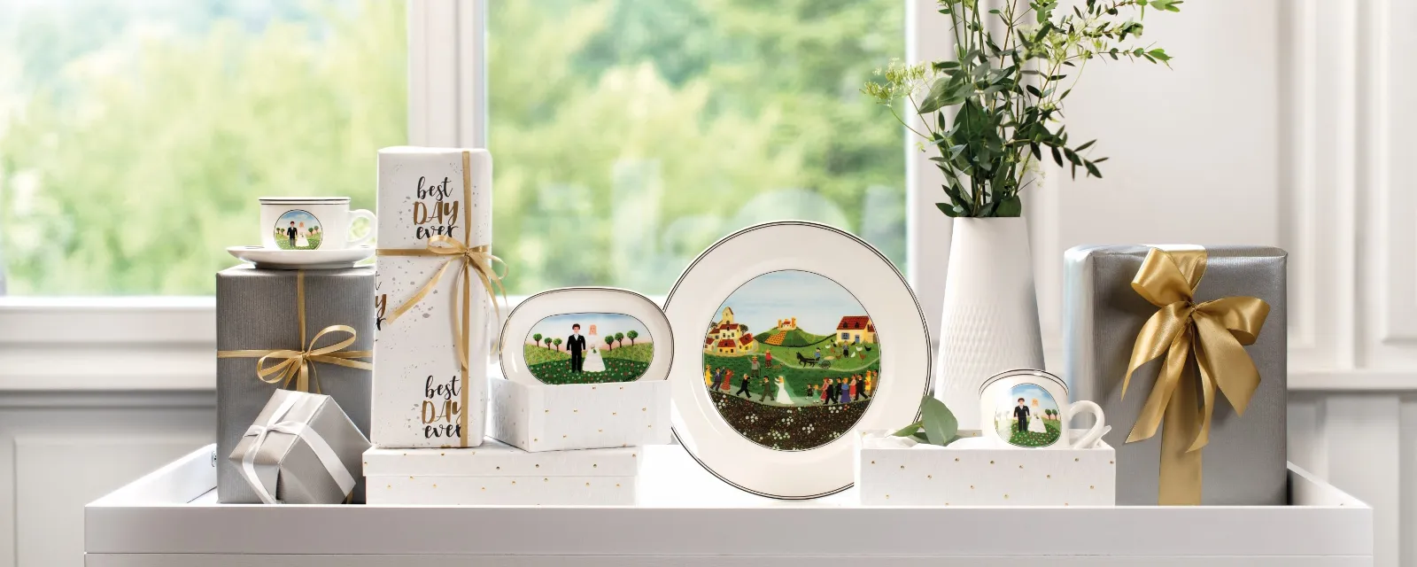 Een Design Naif bord van Villeroy & Boch staat op een tafel versierd met een vaas bloemen, gedecoreerde cadeaus en fotolijstjes voor een raam met uitzicht op de natuur.