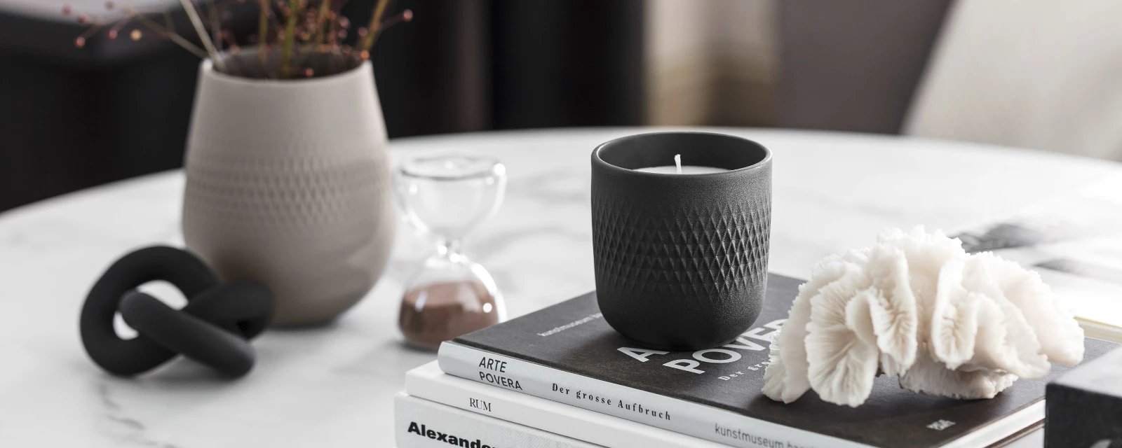 Une élégante composition de décoration intérieure avec une bougie parfumée Manufacture noire, des livres et un vase Manufacture gris clair sur une table en marbre.