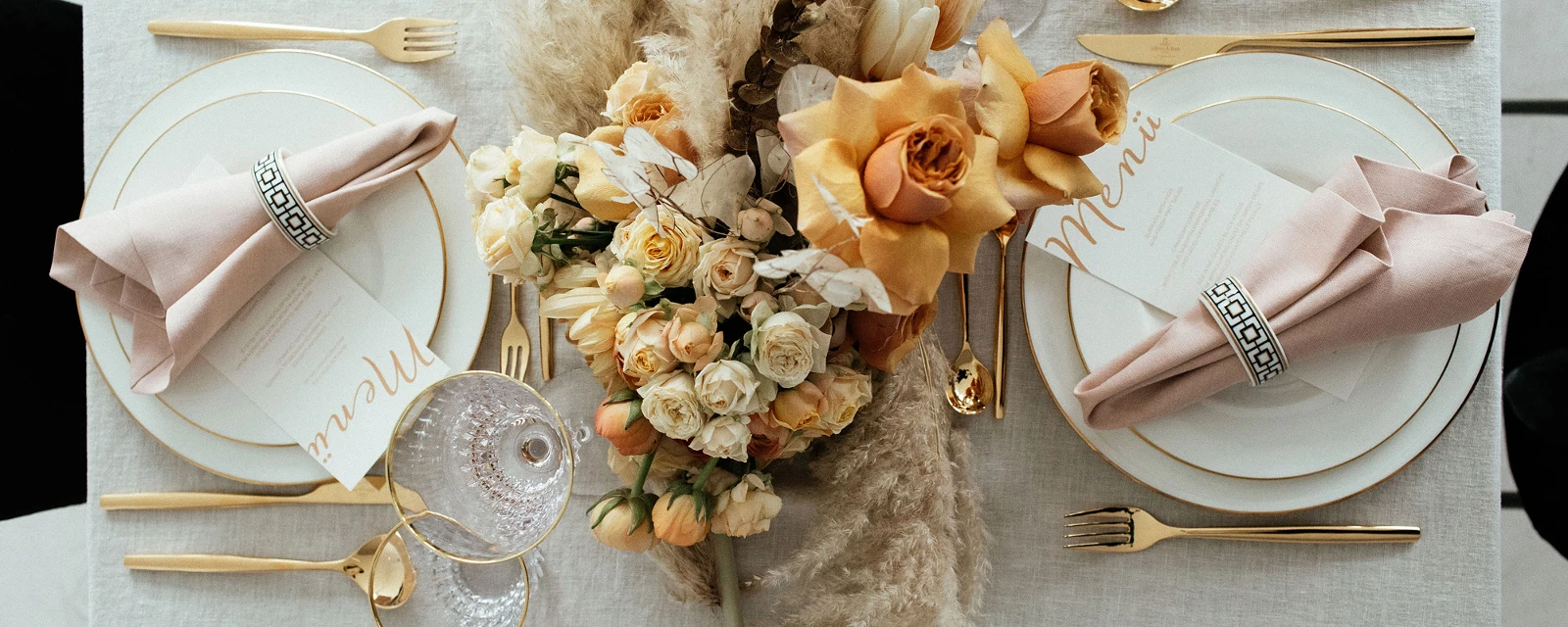 Elegante tafeldecoratie met goudkleurig MetroChic bestek, Anmut servies met gouden rand, floraal center piece en menukaarten.