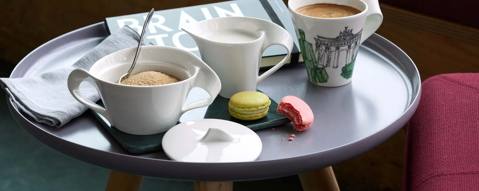 Conjunto de café NewWave con macarons en una mesita Taza de café NewWave, una jarra de leche, un azucarero con cuchara y dos macarons sobre un platillo, en una mesita.