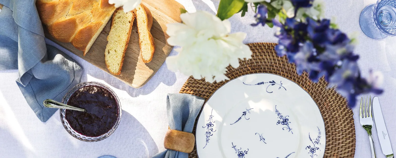 Une assiette Vieux Luxembourg est posée sur une table dressée Sur une table dressée, se trouvent une assiette Vieux Luxembourg de Villeroy & Boch, une serviette en tissu, un couteau, une fourchette et un pot de confiture foncée.