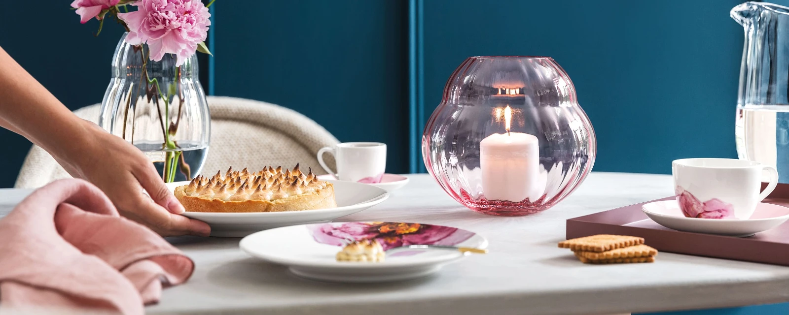 Une table de salle à manger élégante avec une personne servant le dessert, des fleurs fraîches dans des vases Rose Garden et des assiettes de la collection Rose Garden qui accentuent l’ambiance.