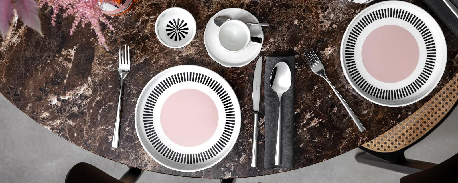 Colour explosion with Memphis by Villeroy & Boch A round marble table with two Memphis place settings, each with a plate, cutlery and a cup. A bowl of apples and a Memphis vase with flowers adorn the center.
