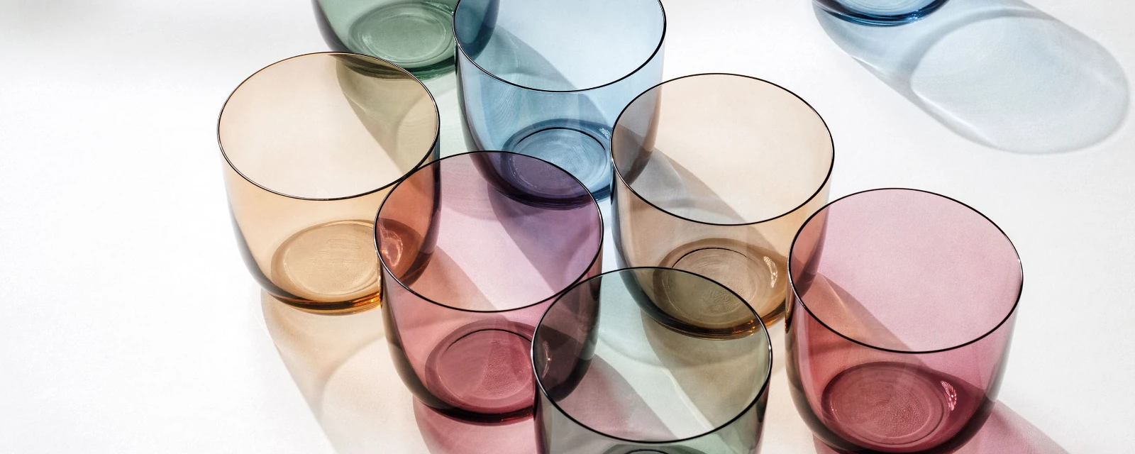 Des verres à eau de différentes couleurs de like. by Villeroy & Boch disposés sur une surface blanche.