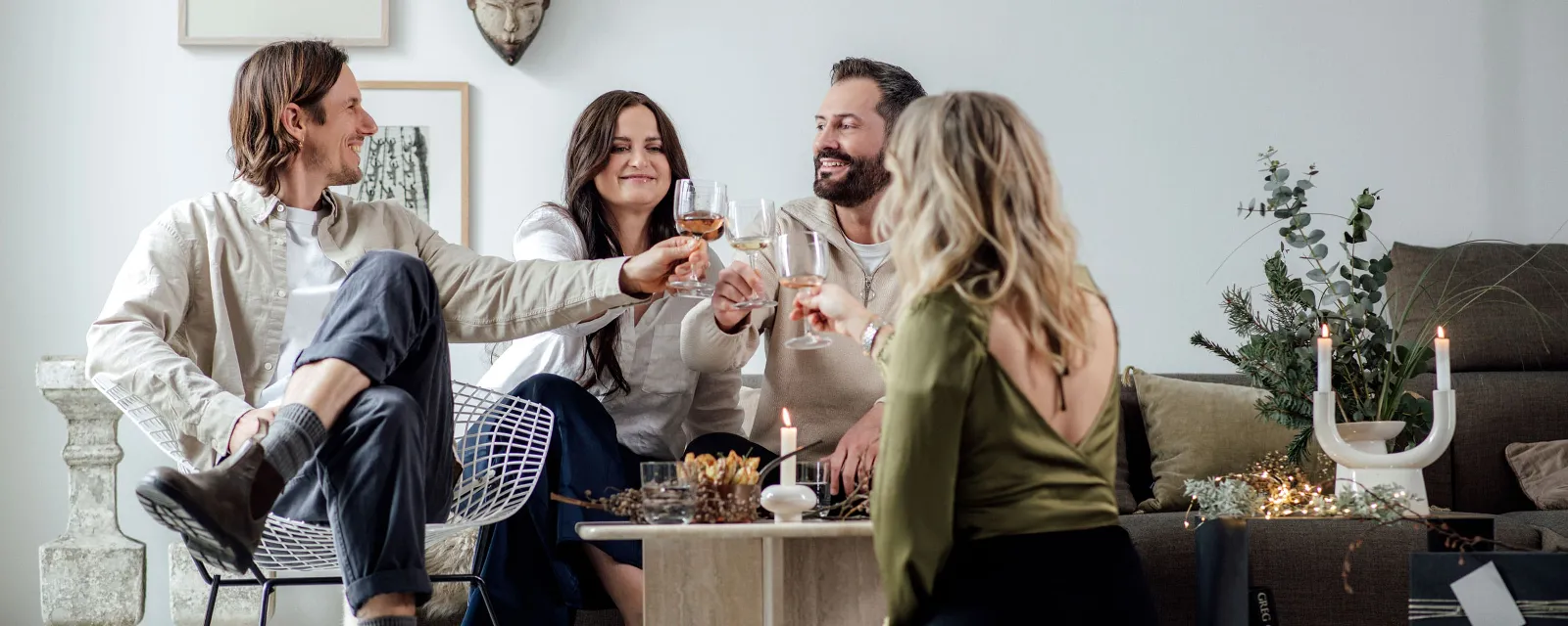Gemütliches Anstoßen mit Winter Glow im Wohnzimmer Vier Personen stoßen mit Winter Glow Gläsern in einem gemütlichen Wohnzimmer an, das mit weihnachtlichen Akzenten dekoriert ist.