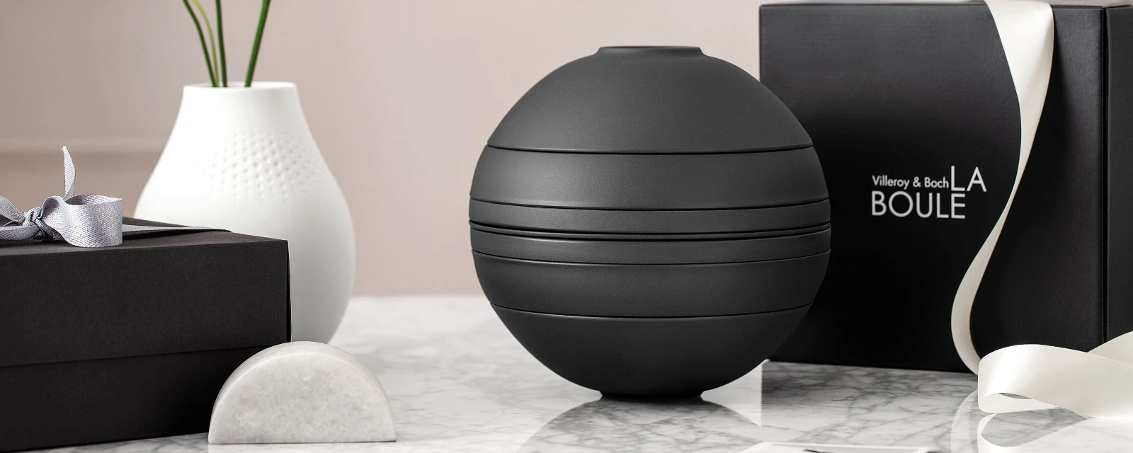 A black La Boule dinnerware set on a table with a black gift box behind it.