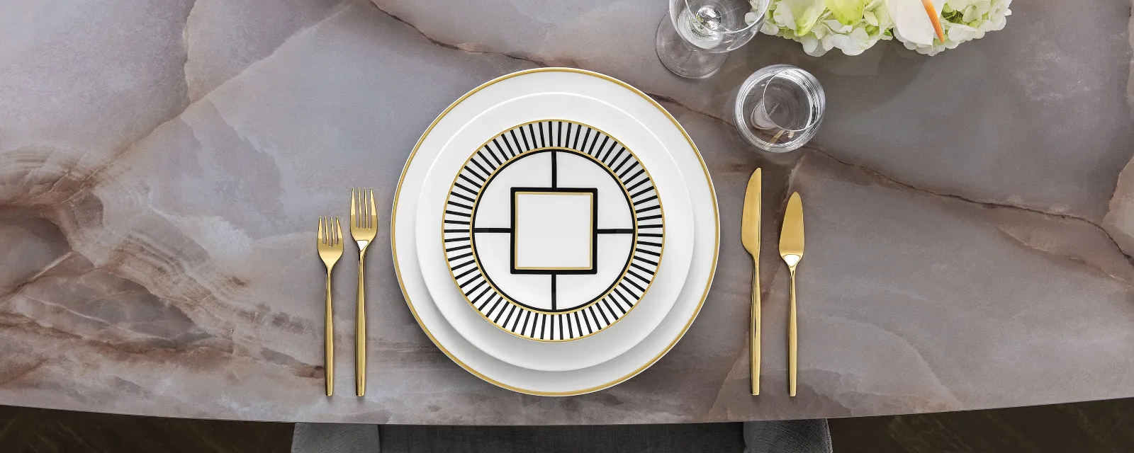 Stylish dinnerware with elegant MetroChic crockery, gold cutlery and a floral centrepiece on a marble table.