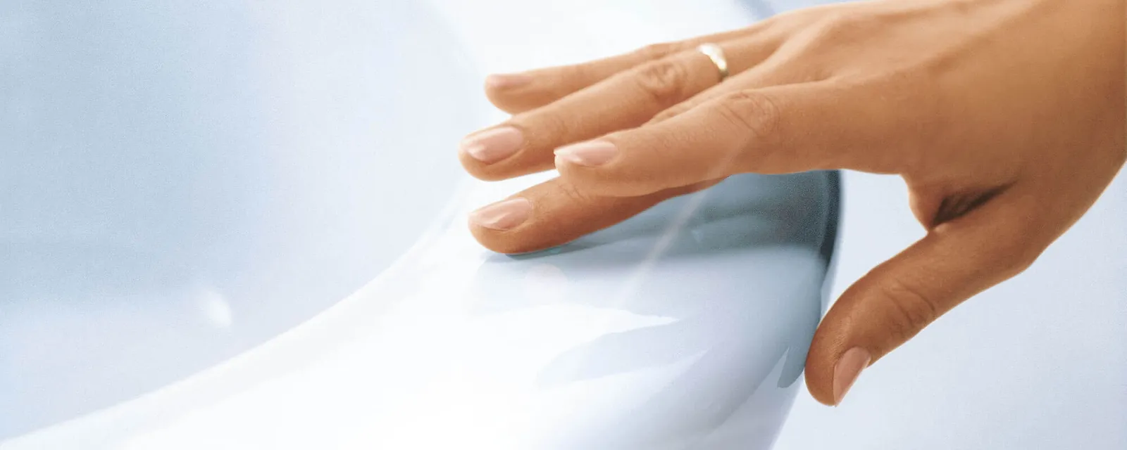 Hand touching a CeramicPlus toilet Close-up of a hand with a gold ring touching the rim of a shiny white ceramic toilet.
