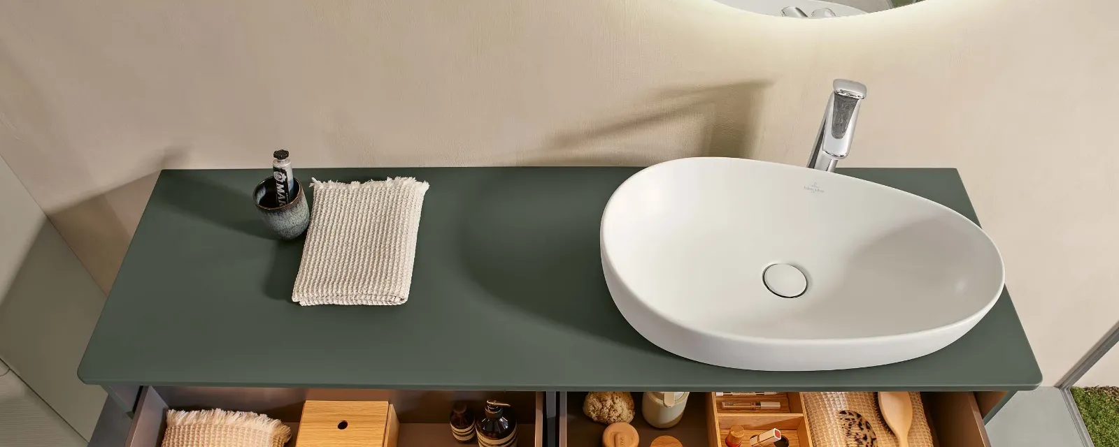 Antao green bathroom console with washbasin A natural green console in a bathroom with two open, full drawers, above which is a freestanding white washbasin from Villeroy & Boch Antao.
