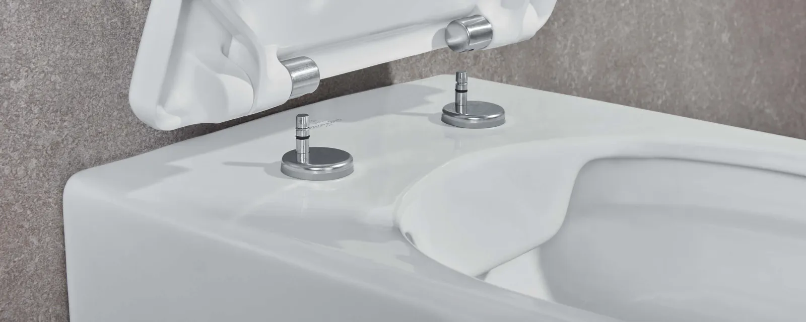 Mocowanie deski sedesowej Villeroy & Boch Osoba mocuje białą deskę sedesową do muszli klozetowej za pomocą dwóch metalowych śrub i zawiasów.