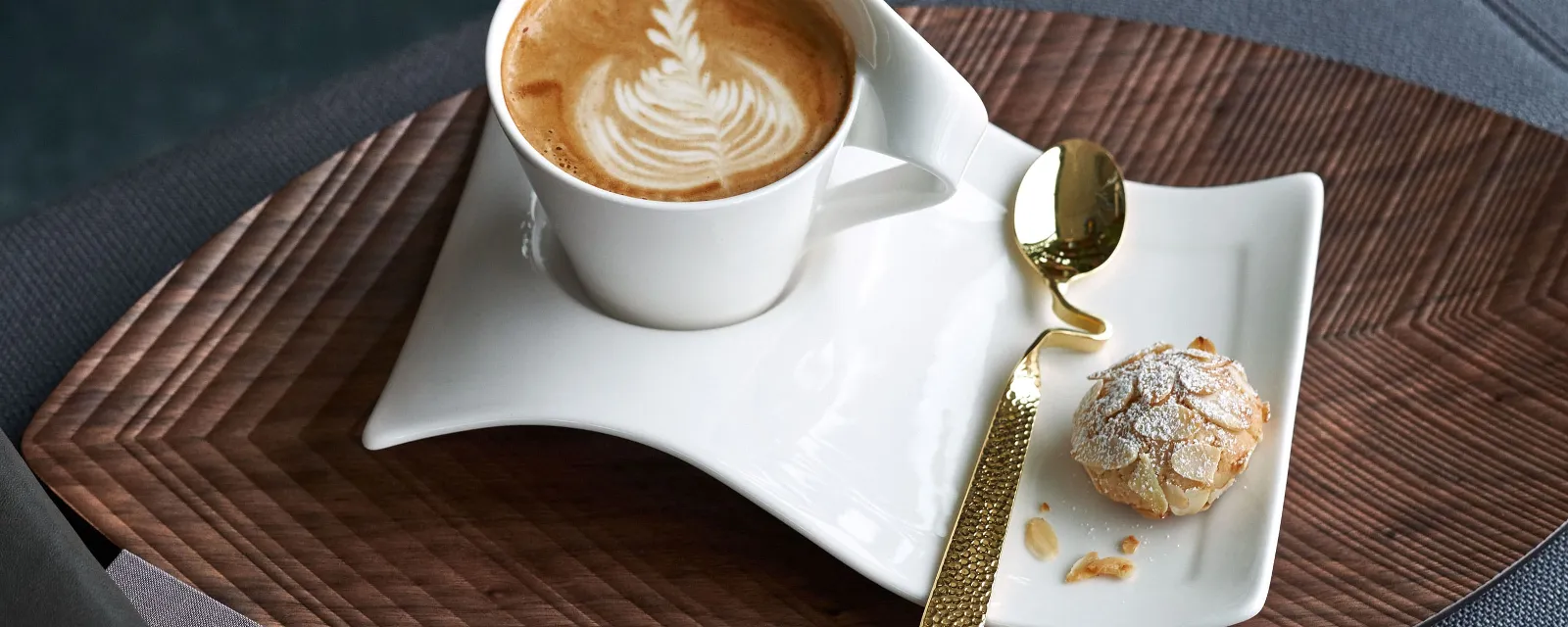 Trevlig kaffepaus med NewWave-kopp och sofistikerad sked En NewWave-kopp med Latte Art och kakor på ett träbord, tillsammans med en sofistikerad NewWave-sked.