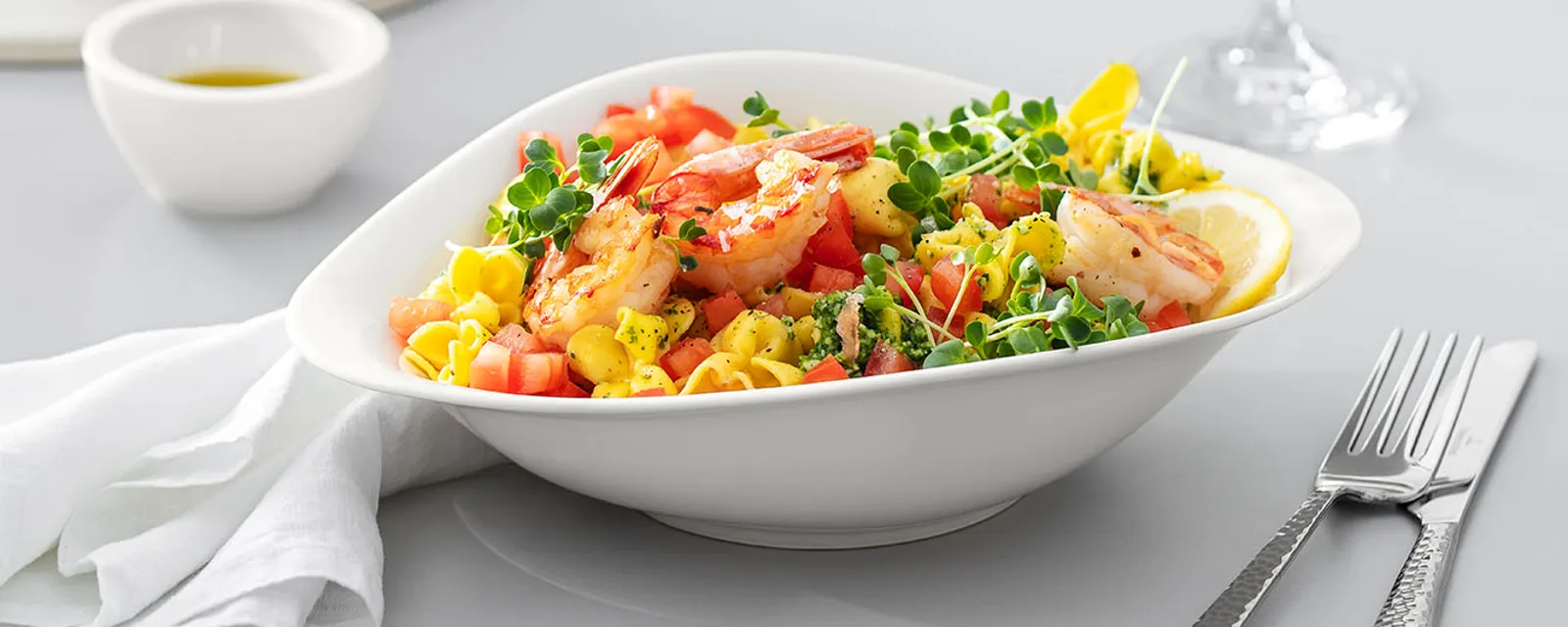 Vapiano bord van Villeroy & Boch op een houten tafel gevuld met pastasalade. Een wijnglas en bestek van Villeroy & Boch op tafel 