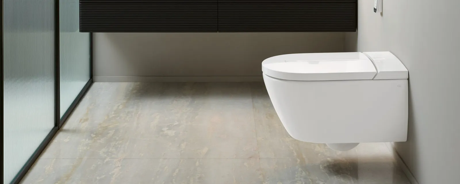 Bagno moderno con WC a parete, lavabo nero sospeso con bacino bianco, specchio rotondo illuminato, lampade a sospensione e divisorio in vetro smerigliato.