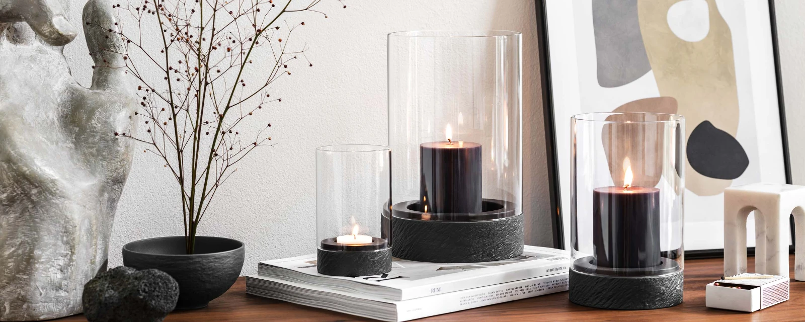 A modern home interior with a wooden sideboard and dried flower with three Manufacture hurricane lamps.