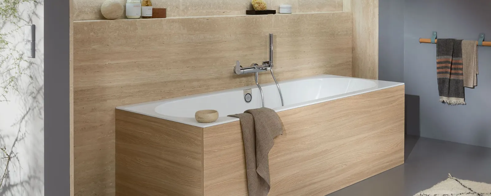 Modernes Badezimmer mit einer eckigen holzverkleideten Badewanne, eingebauten Regalen mit Dekor und Toilettenartikeln, einem seitlich hängenden Handtuch und einer sanften, neutralen Farbpalette.