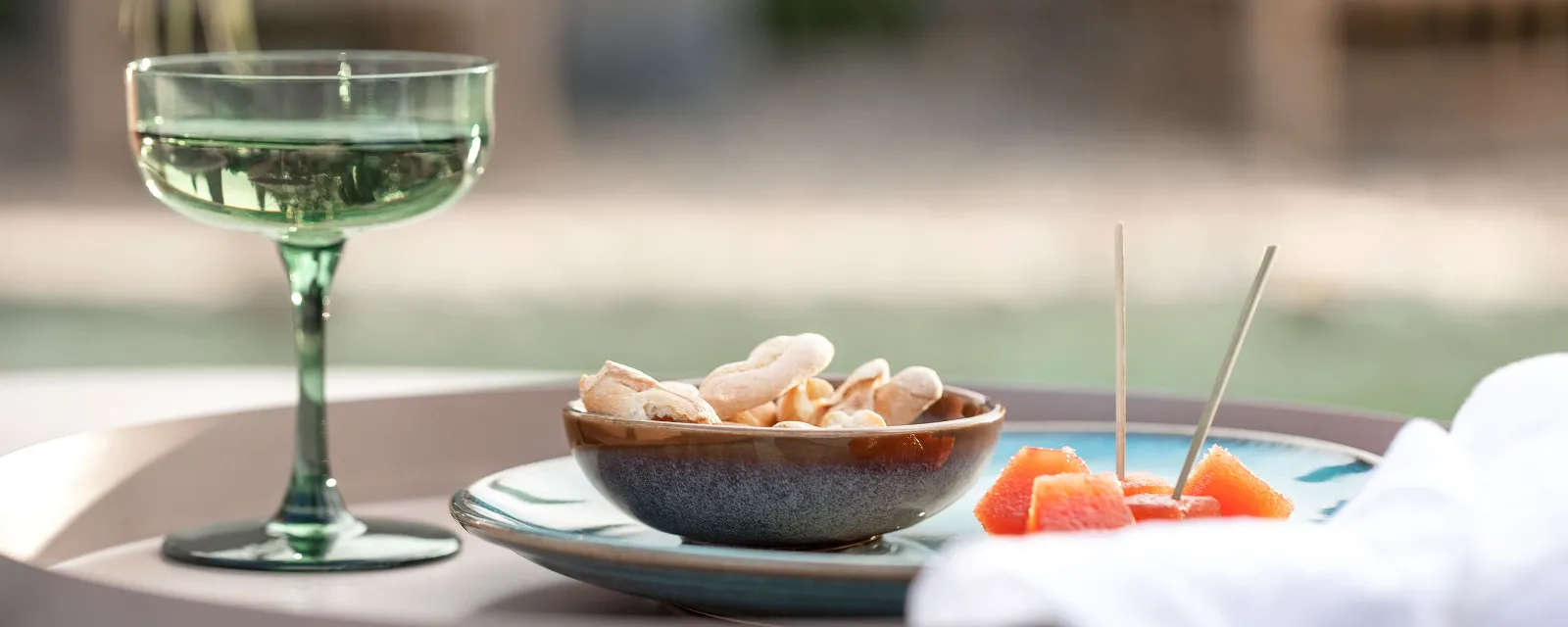 Een Like Sage glas, een Lave schaal met crackers en sinaasappelschijfjes op een dienblad buiten.