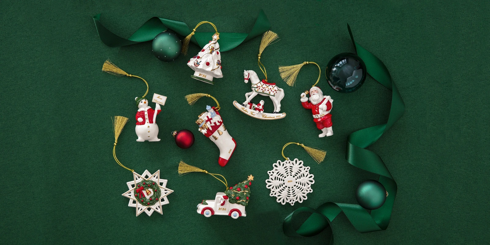 Annual 2024 Christmas ornaments including Santa, a snowflake, and a rocking horse, arranged on a green background with green ribbon and spherical decorations