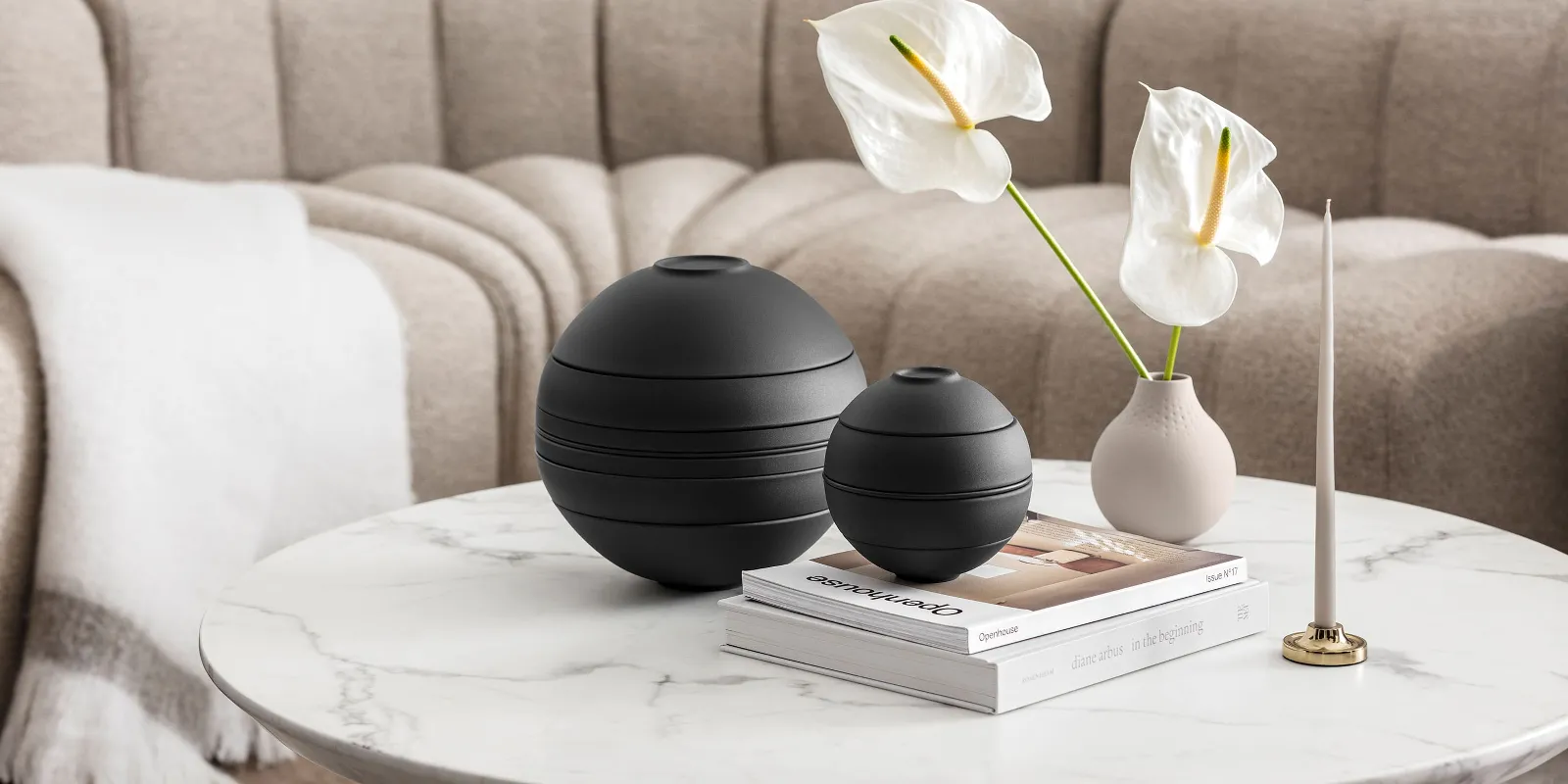 La Boule nera di Villeroy & Boch, un vaso beige con fiori bianchi, un portacandele e alcuni libri in un ambiente beige.