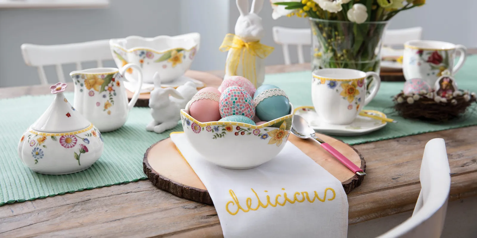 Una tavola colorata per il brunch di Pasqua con stoviglie floreali della collezione Spring Awakening, con una statuetta di coniglietto e uova dipinte in modo vivace in una ciotola.