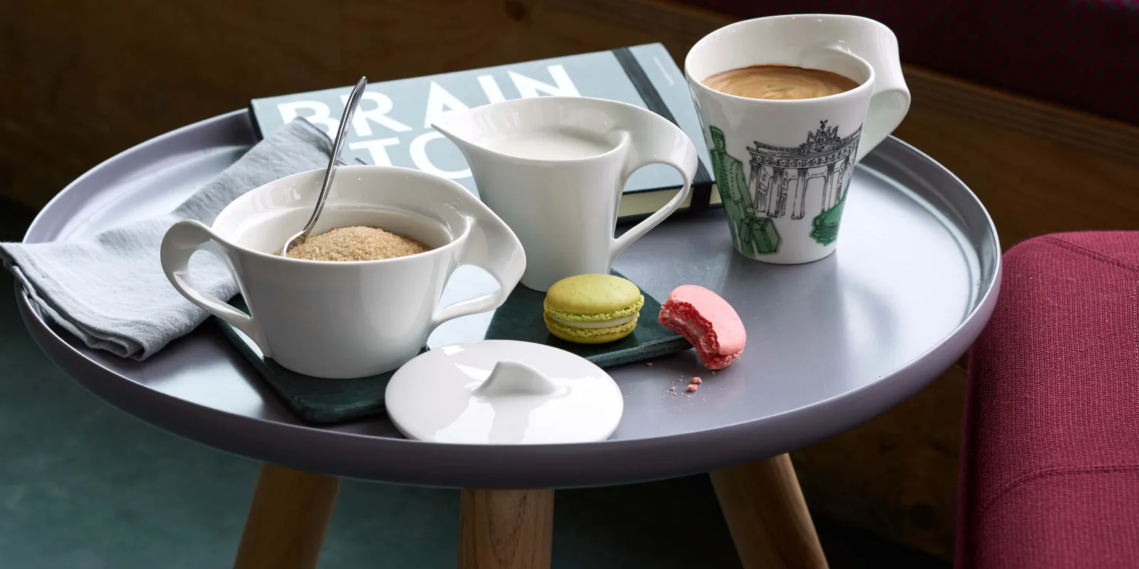 NewWave koffiekopje, een melkkannetje, een suikerpotje met lepeltje en twee macarons op een schoteltje, op een tafeltje.