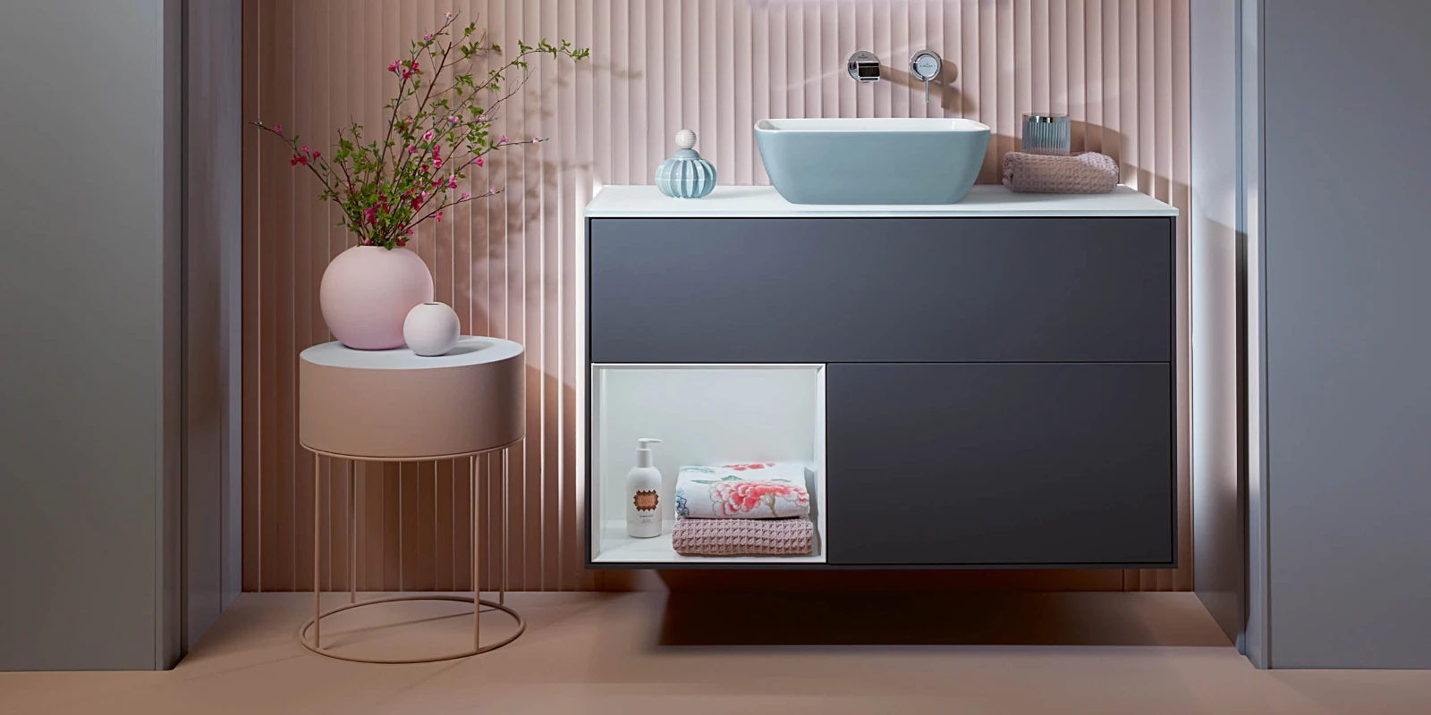 Mobile sottolavabo blu scuro Finion di Villeroy & Boch in un bagno rosa con tavolino rosa.