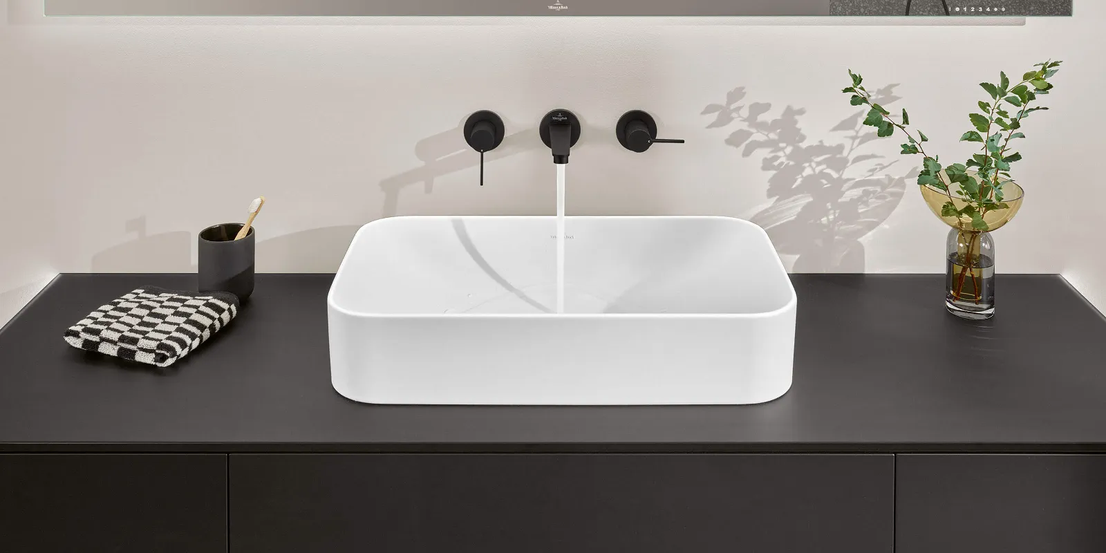 Lavabo da bagno moderno con design quadrato su piano nero, rubinetto cromato e pianta decorativa