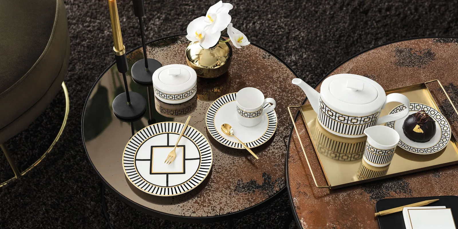 MetroChic tea set on a round table with gold accents, accompanied by orchids, candles and small snacks.