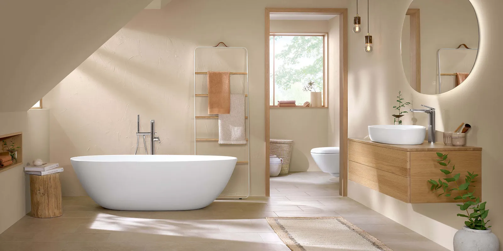 Bagno con interni moderni, con vasca free-standing, lavabo in legno con piano d'appoggio, WC, specchi rotondi e pareti beige, con luce naturale che entra da una porta aperta.