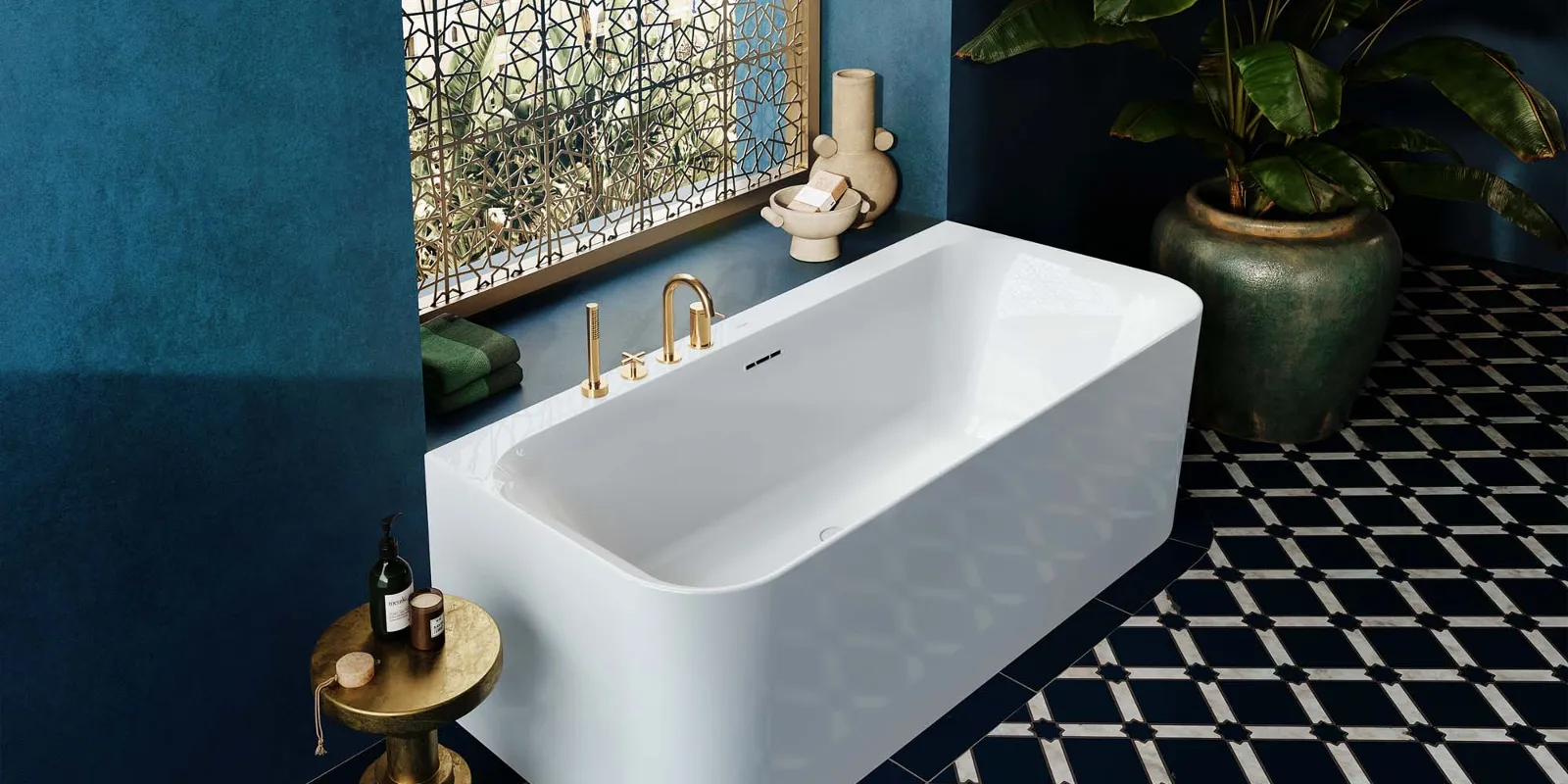 Ein luxuriöses Badezimmer mit einer  Vorwand-Badewanne aus der Loop & Friends Kollektion von Villeroy & Boch. Die Wanne ist weiß und hat goldene Armaturen. Das Bad ist in tiefem Blau gehalten, mit gemusterten Fliesen am Boden.