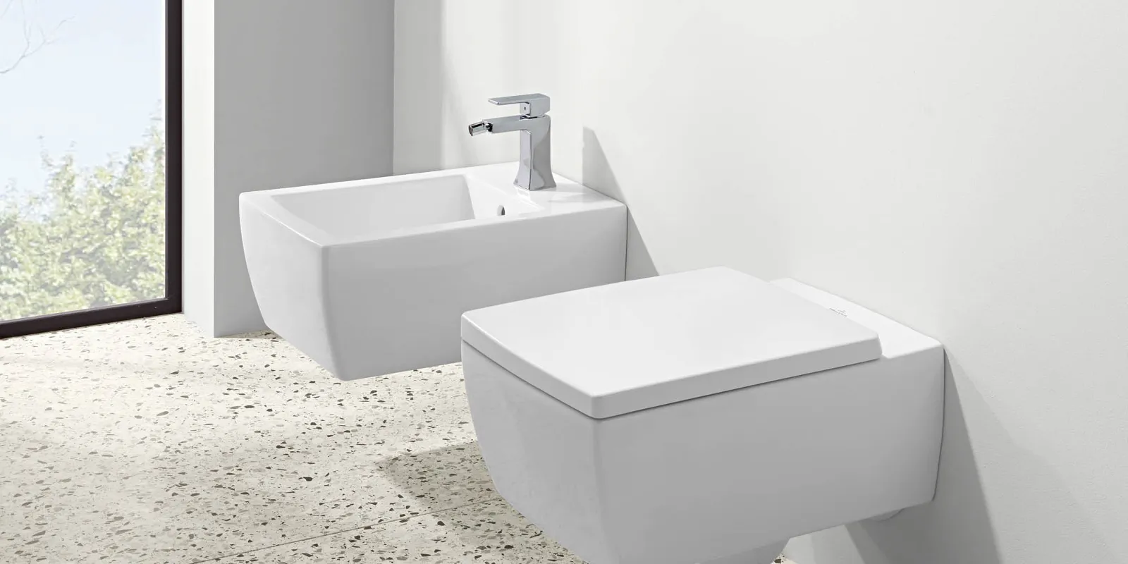 Arredo bagno moderno e minimalista con bidet e WC bianchi davanti a un'ampia finestra