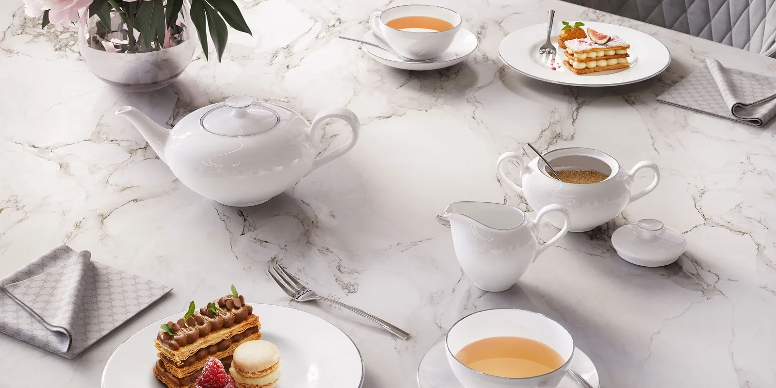 Elegant Anmut tea setting on a marble table, consisting of a teapot, cups and a milk jug with tea and pastries.