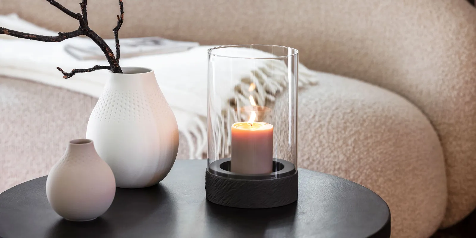 A Manufacture candle stands on a table next to two Manufacture vases.