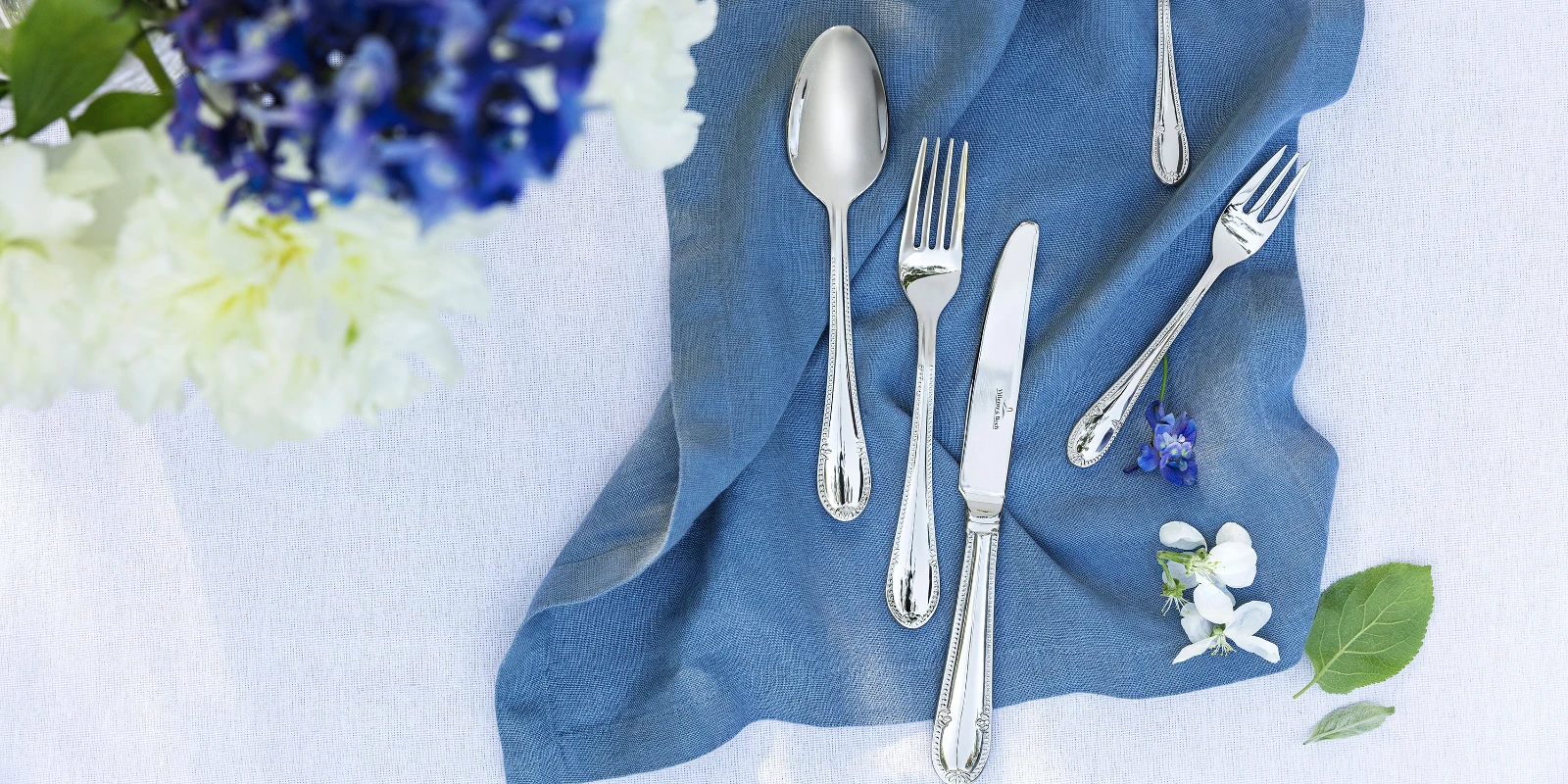 Eleganti decorazioni per la tavola con le posate Mademoiselle su un tovagliolo di lino blu e un bouquet di fiori.