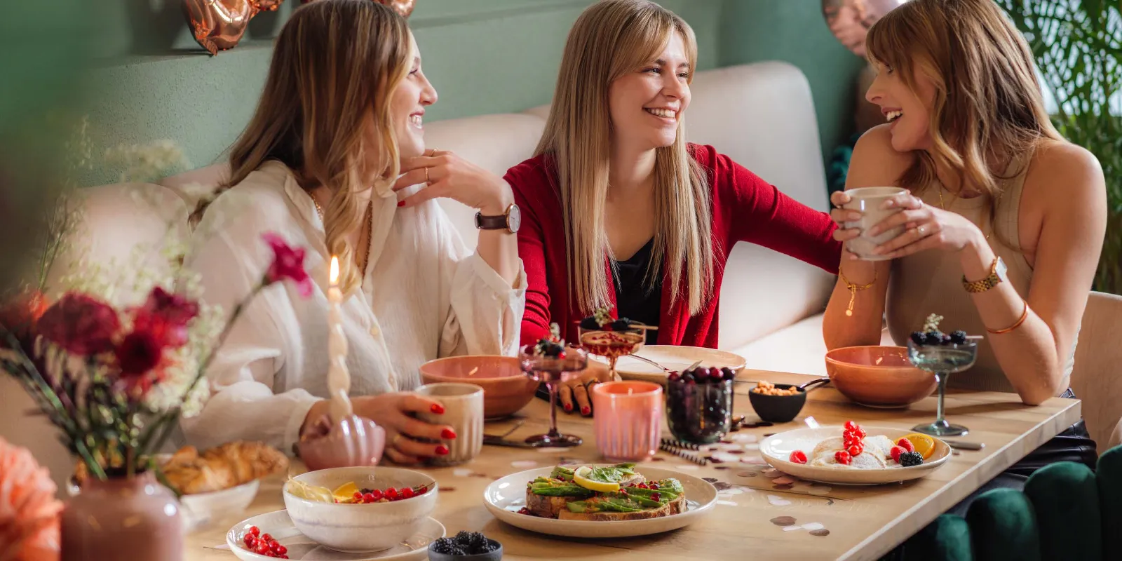 A festive scene with three women at a table with Perlemor dinnerware and Like glass from like. by Villeroy & Boch, and balloons in the background.