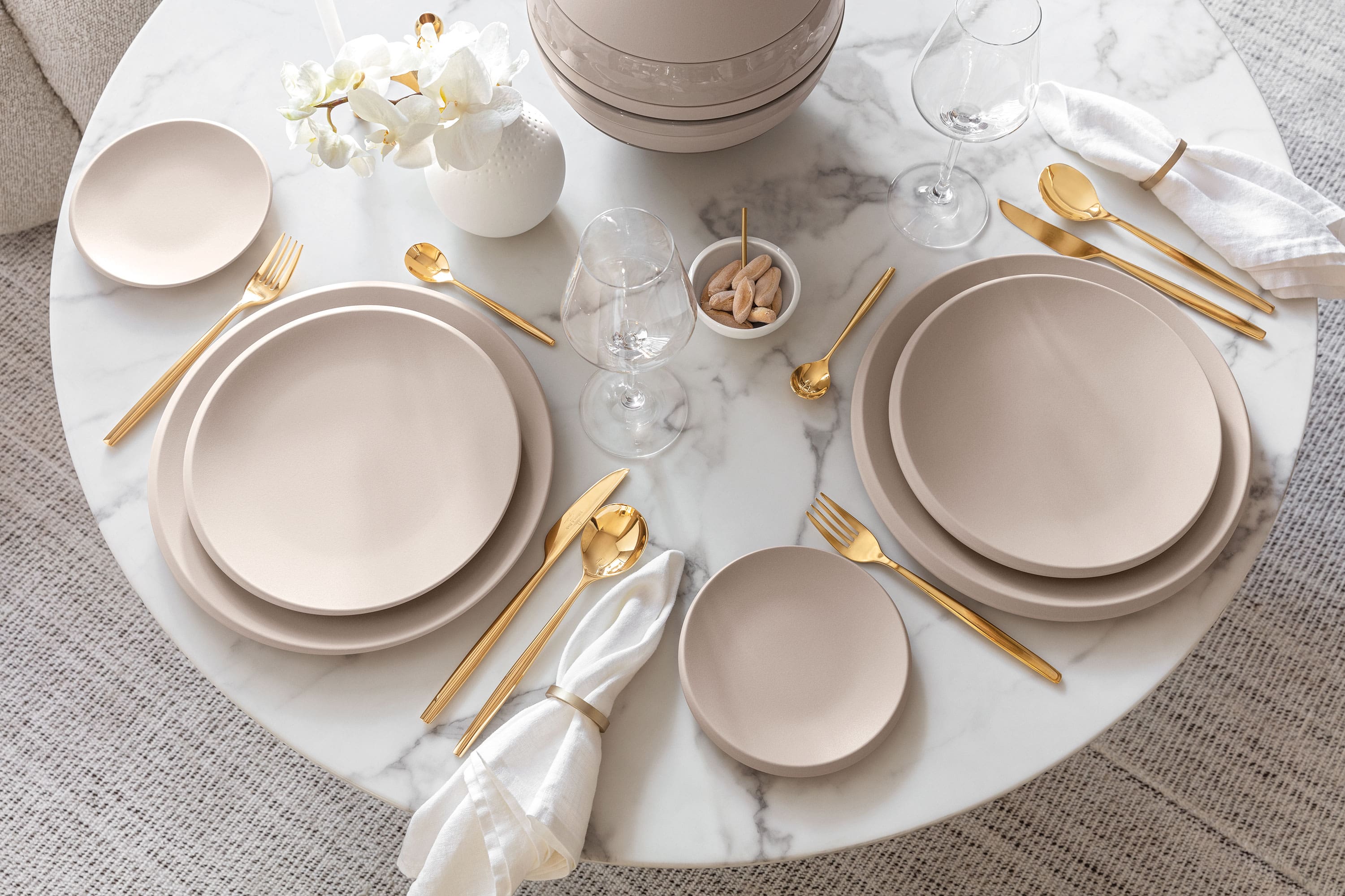 Een gedekte tafel met beige NewMoon borden en gouden MetroChic bestek van Villeroy & Boch.