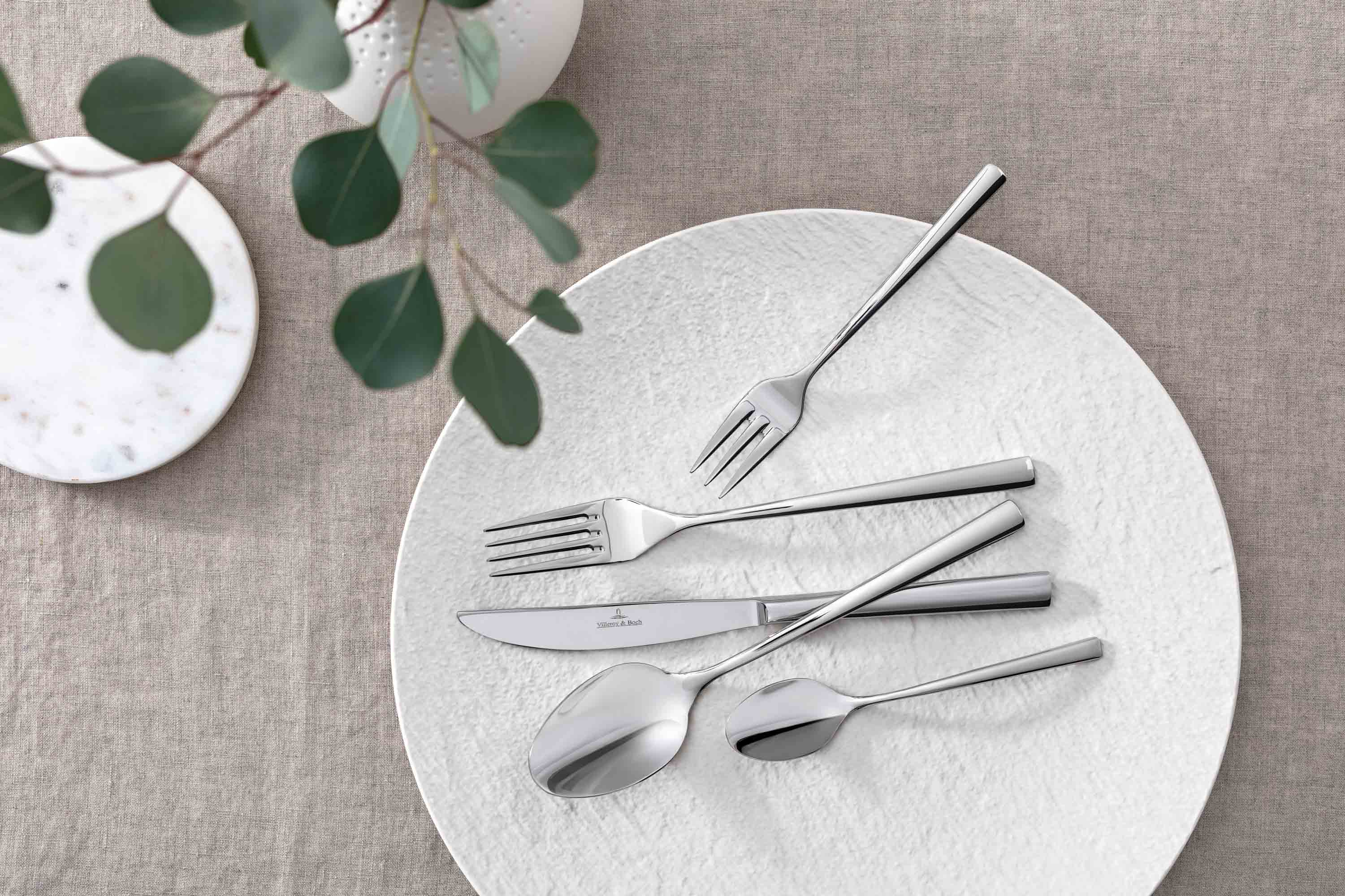 Elegant table decor with modern Piemont flatware and decorative green on a neutral table cloth.