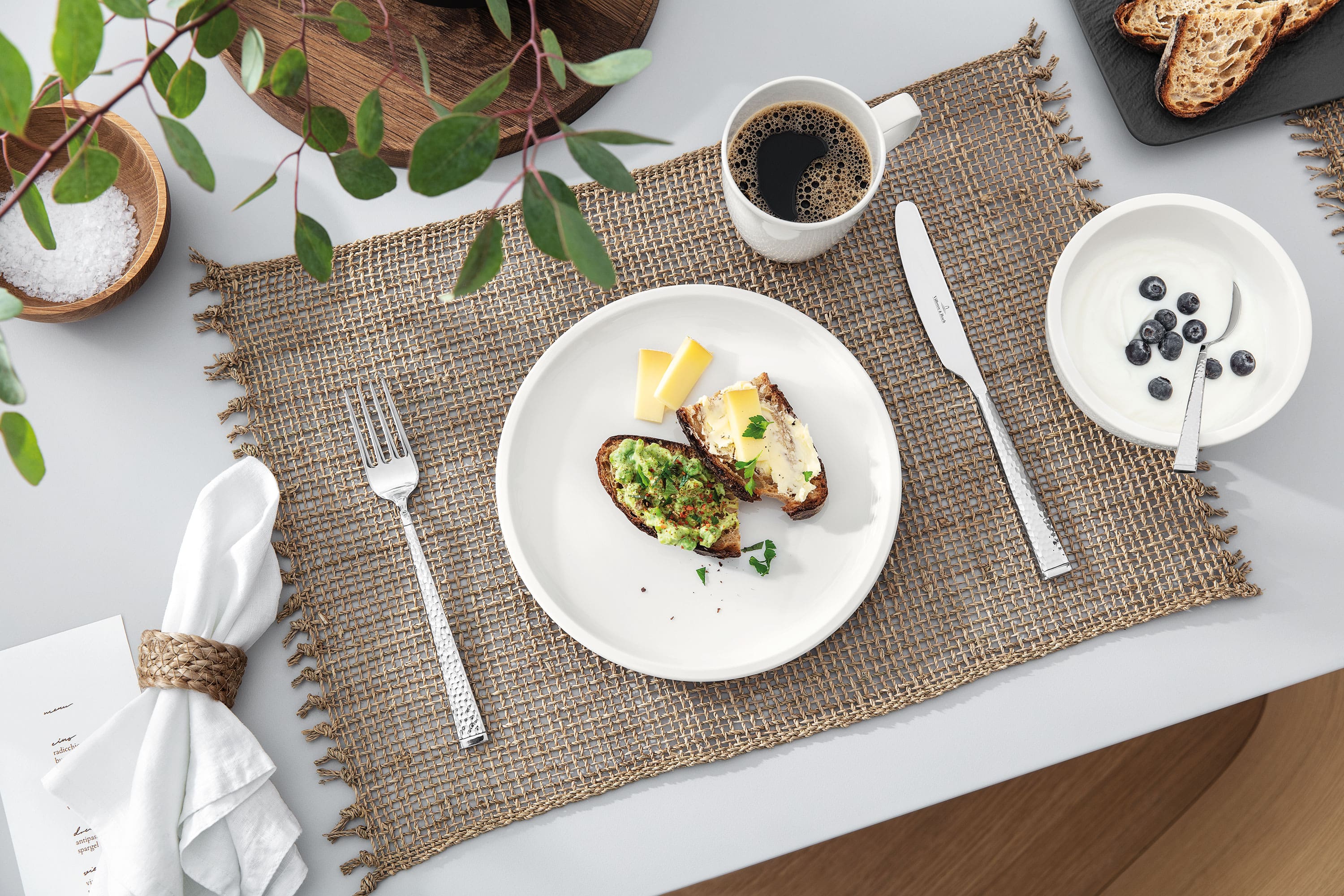 Une table dressée avec une tasse à café et une assiette Artesano blanche de Villeroy & Boch avec de la nourriture.