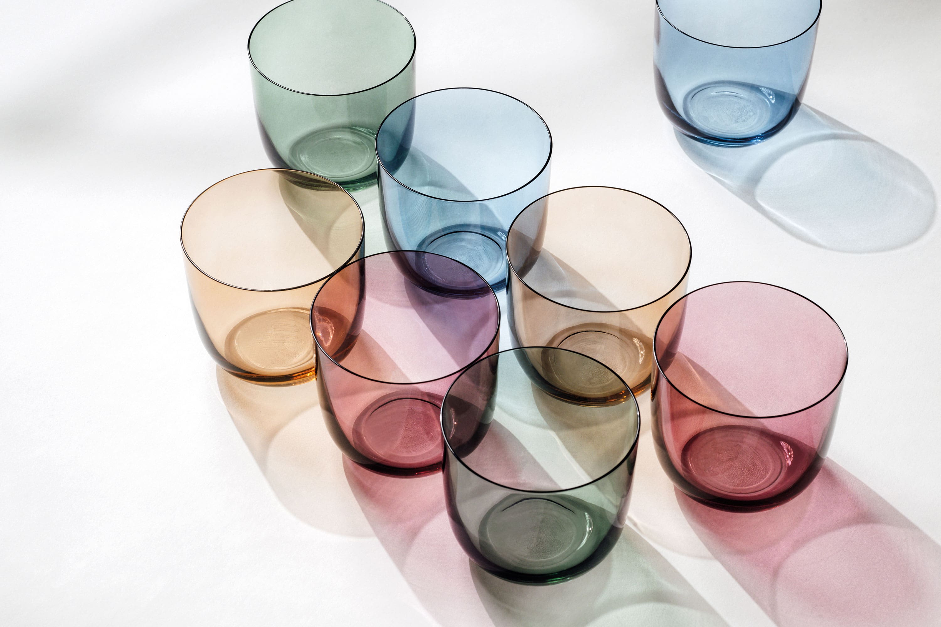 Water glasses in different colors from like. by Villeroy & Boch arranged on a white surface.