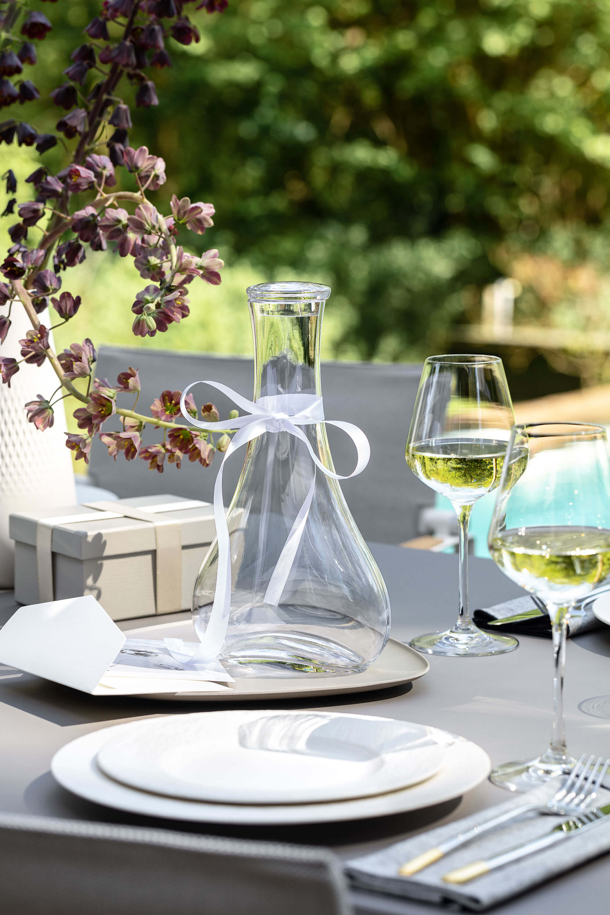 An elegant Purismo wine decanter with a white bow and wine glasses on a table.