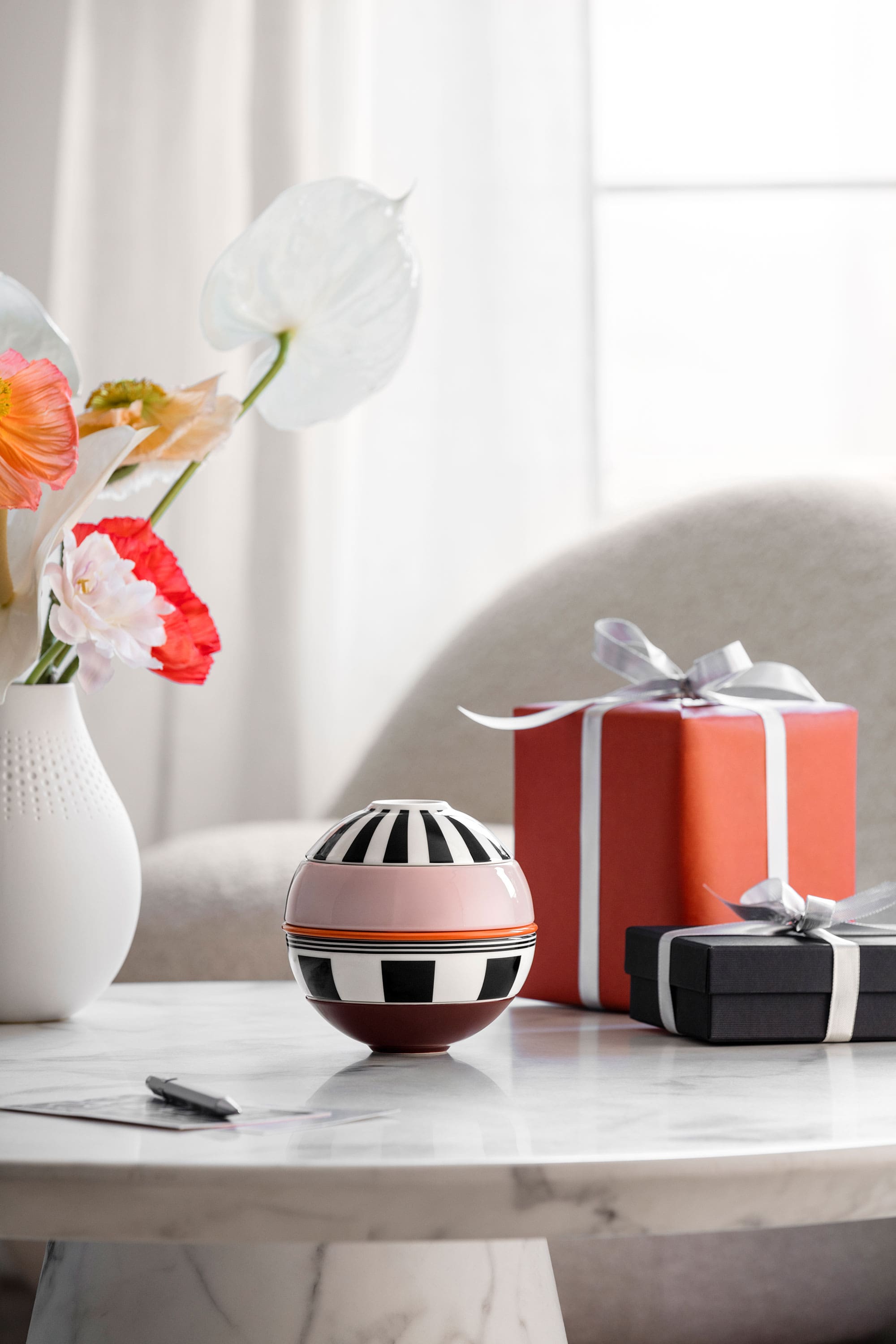 La petite Boule Memphis from Villeroy & Boch and two wrapped gifts stand on a marble table, with a vase of flowers in the background.
