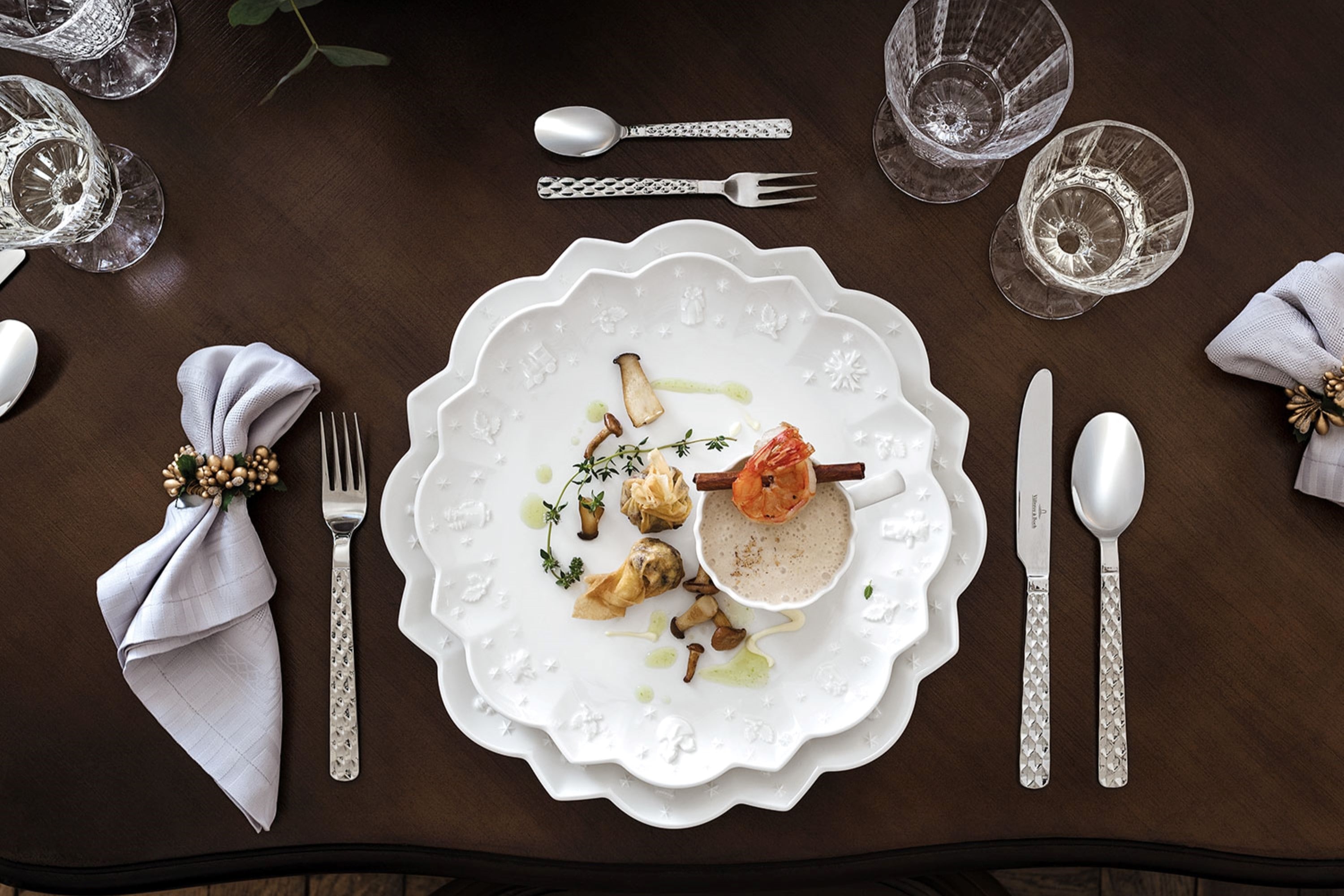 Boston cutlery with Toy's Delight Christmas dinnerware A sophisticated dining table arrangement presenting the Villeroy & Boch "Boston" plates, which are artfully decorated with a wave pattern, together with crystal glasses, richly decorated silver cutlery and decorative napkins on a dark wooden table.