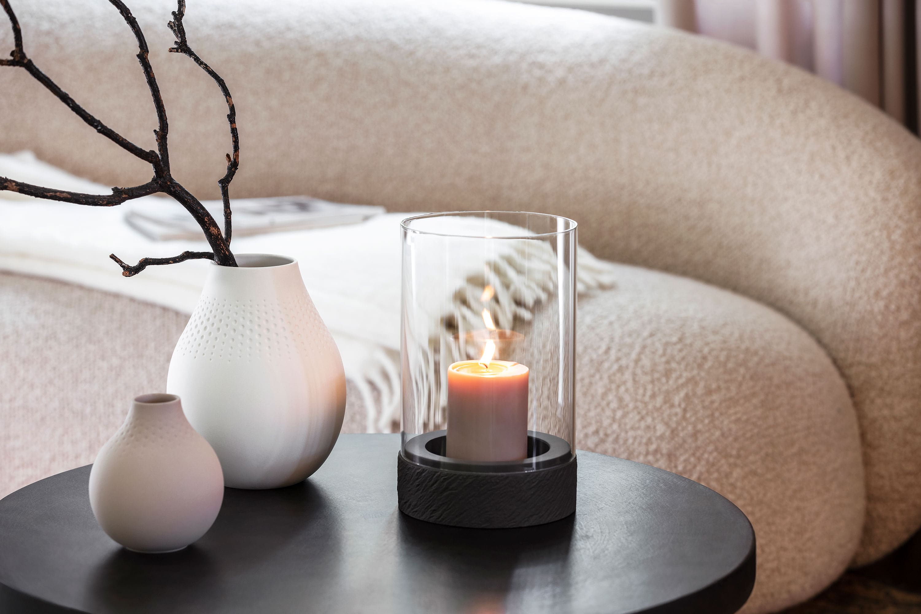 A Manufacture candle stands on a table next to two Manufacture vases.