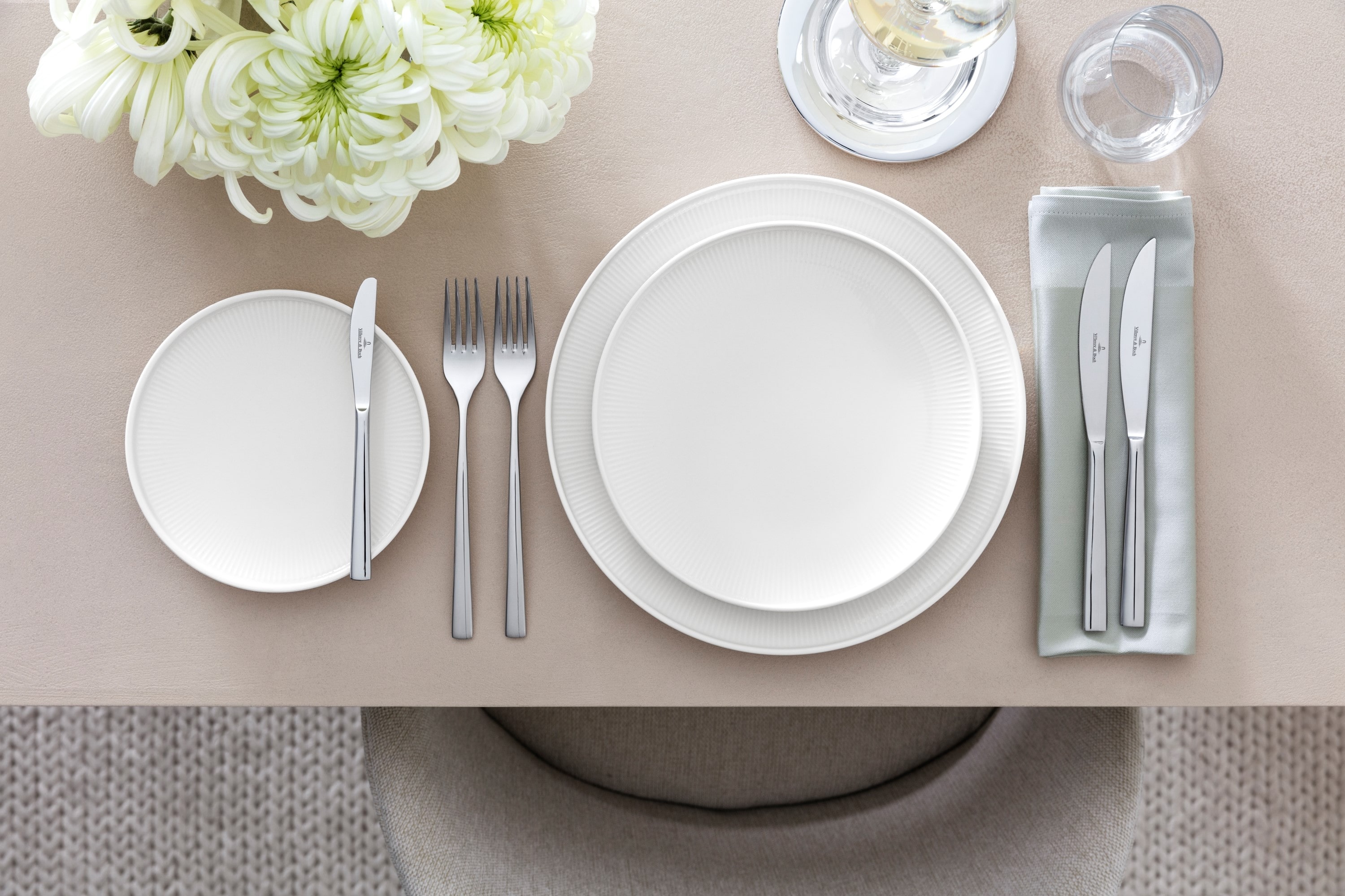 Sophisticated table arrangement with the Piemont collection from Villeroy & Boch, including a white dinner plate, a salad plate, a flatware set, glassware, and a floral centerpiece on a beige tablecloth.