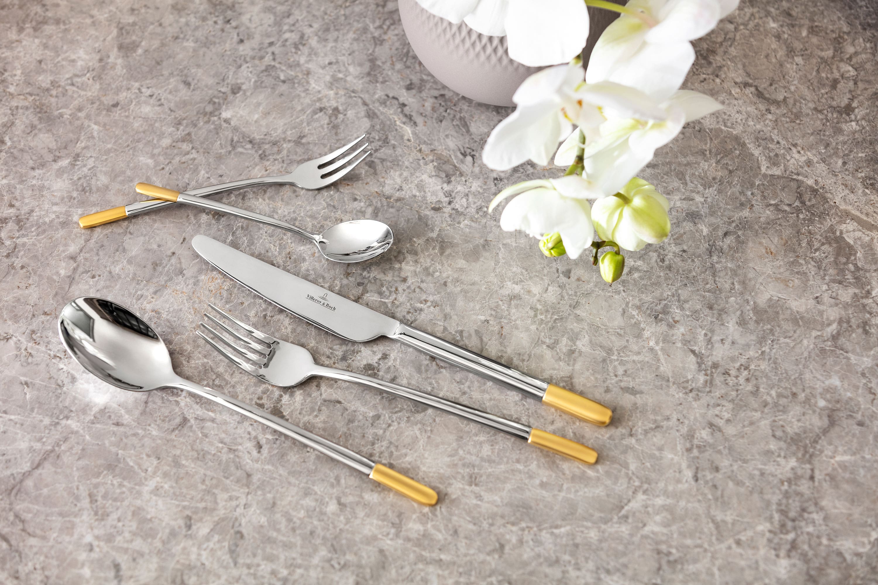 Elegant Ella flatware set with golden accents on a marble tabletop, accompanied by a white orchid.